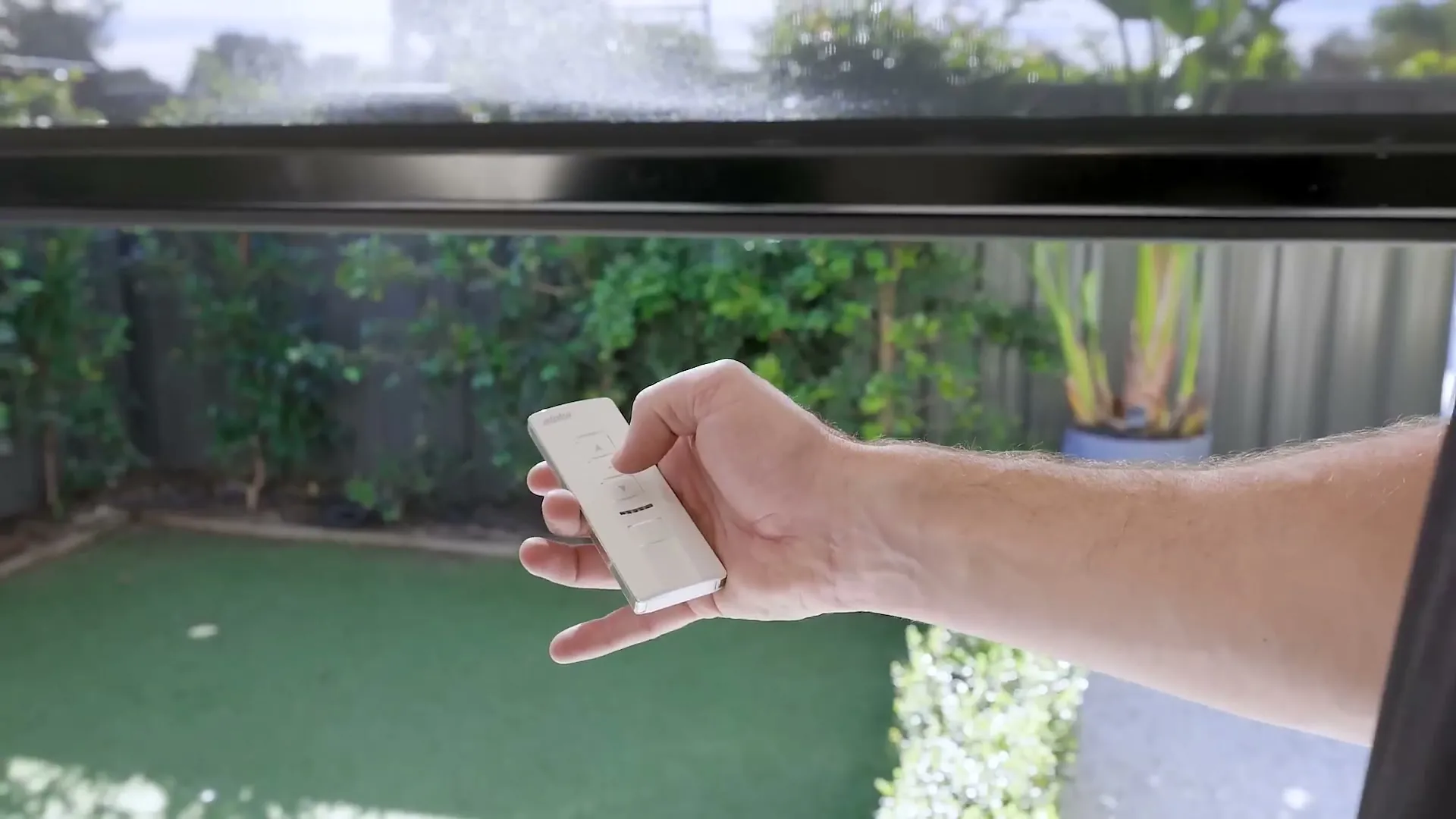 Hand holding a remote to operate motorised outdoor blinds over a Perth courtyard
