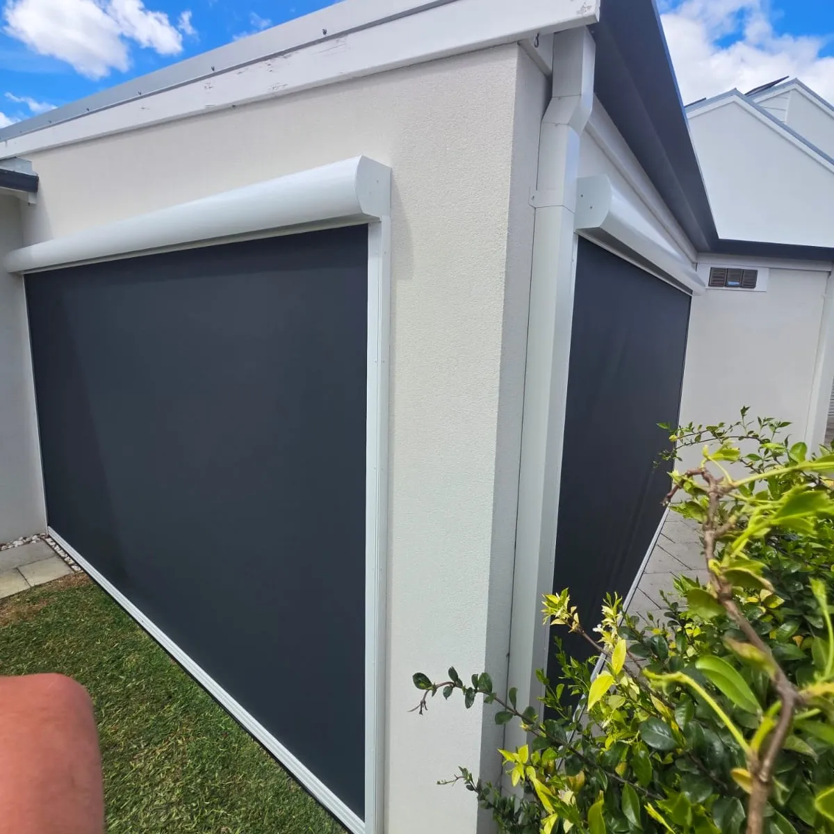 Charcoal Slidetrack blinds on a white rendered alfresco corner with hedging